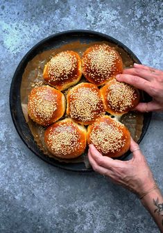 a person is placing sesame seed on top of buns in a skillet with one hand