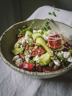 a salad with tomatoes, cucumbers and feta cheese in a white bowl