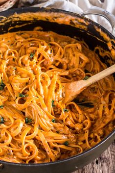 a skillet filled with pasta and sauce on top of a wooden table next to bread