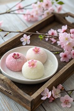 three desserts are sitting on a plate with pink flowers in the background and wooden tray