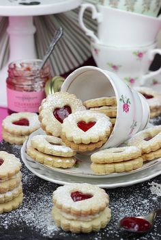 heart shaped cookies are on a plate next to cups and saucers with jam in them