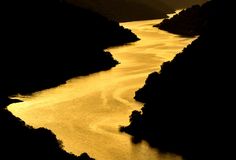 the sun shines brightly over a river as it flows through some hills and trees