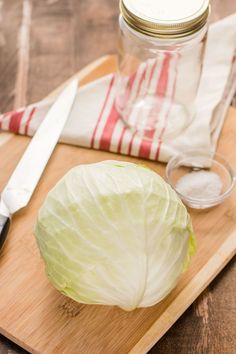 a head of cabbage sits on a cutting board next to a knife, salt and pepper shaker