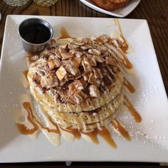 pancakes covered in caramel drizzle on a white plate with syrup and sauce