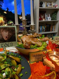 a table topped with plates of food next to candles and pictures on bookshelves