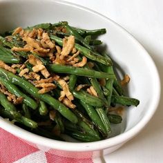 a white bowl filled with green beans covered in toppings on top of a red and white checkered table cloth