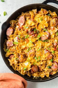 a skillet filled with pasta, sausages and cheese on top of a table