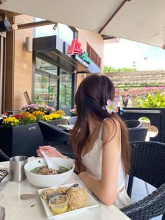 a woman sitting at a table in front of a bowl of food with a flower in her hair