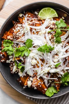 a skillet filled with food and garnished with cilantro, onions, parmesan cheese and lime