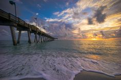 the sun is setting over the ocean with a pier stretching into the distance from the water