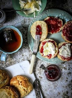 scones with jam and butter are on plates next to a cup of tea, spoon and knife