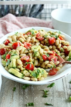 a white bowl filled with beans, tomatoes and avocado on top of a wooden table