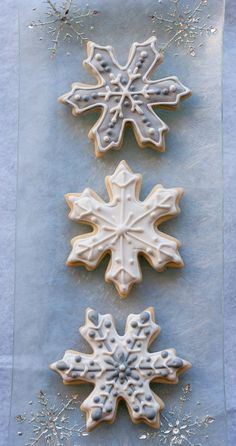 three snowflake cookies sitting on top of a blue table covered in frosting