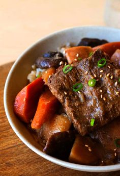 a white bowl filled with meat and vegetables on top of a wooden table next to a glass of water
