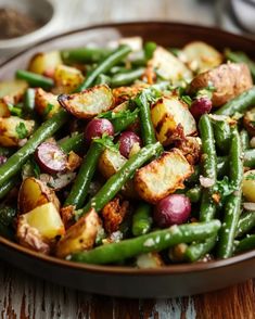 a bowl filled with green beans, potatoes and other vegetables on top of a wooden table