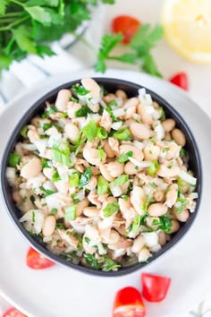 a bowl filled with beans and vegetables on top of a white plate next to tomatoes