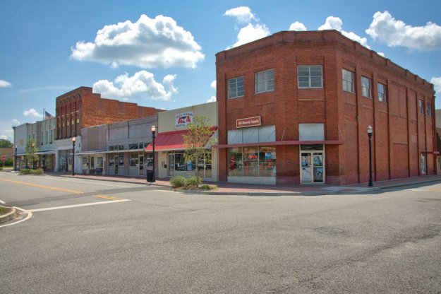 A street view of a historic downtown area with brick buildings, storefronts, and decorative lampposts under a blue sky with fluffy clouds.