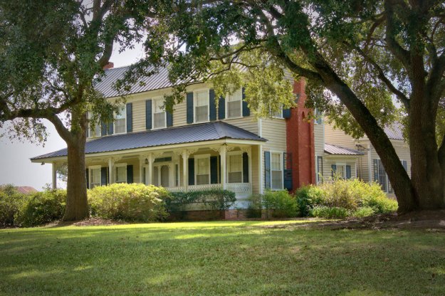A large two-story house with a porch, surrounded by trees and greenery.