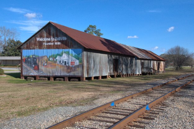 Rusted freight depots along the railroad tracks in Bellville, Georgia, with a colorful mural on the end of one building.