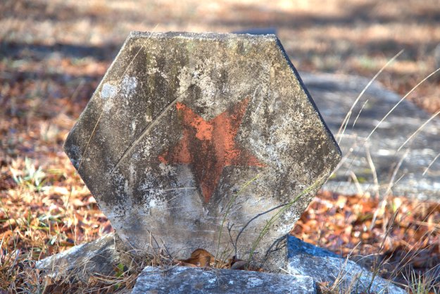 A weathered hexagonal stone marked with a faded red star, surrounded by dry grass and fallen leaves.