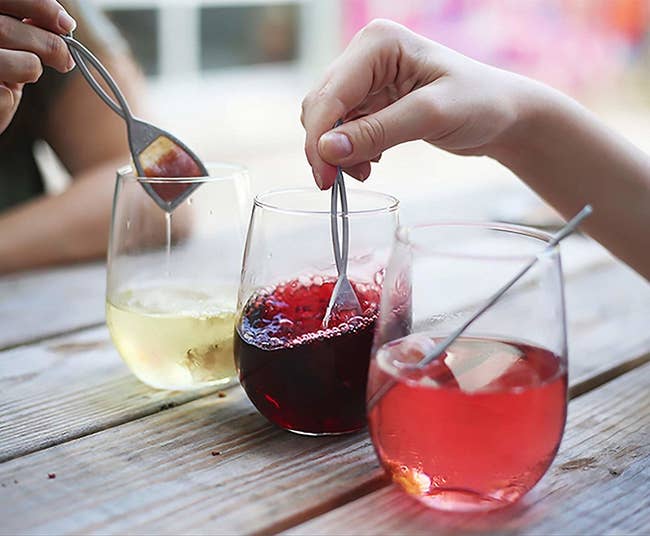 hands dip tea bag like devices into wine