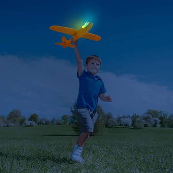 A child playing with the lit up orange plane at night