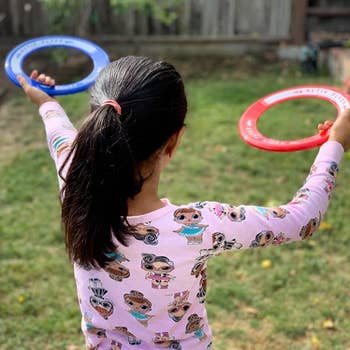 reviewer showing their child holding the red and blue flying rings in the yard