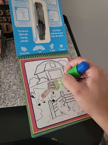 Hand using a green marker to color barn animals on a farm-themed children's coloring book