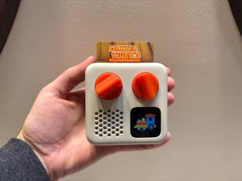 Hand holding a child-friendly radio device with red knobs and a small screen, featuring
