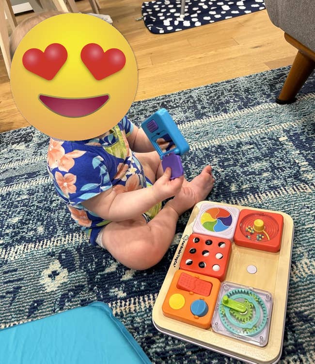 Baby in a floral-patterned outfit plays with a wooden activity toy on a rug