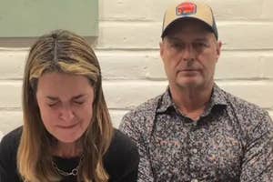 Two people sitting indoors. The woman appears emotional with eyes closed; the man is looking forward. Casual attire