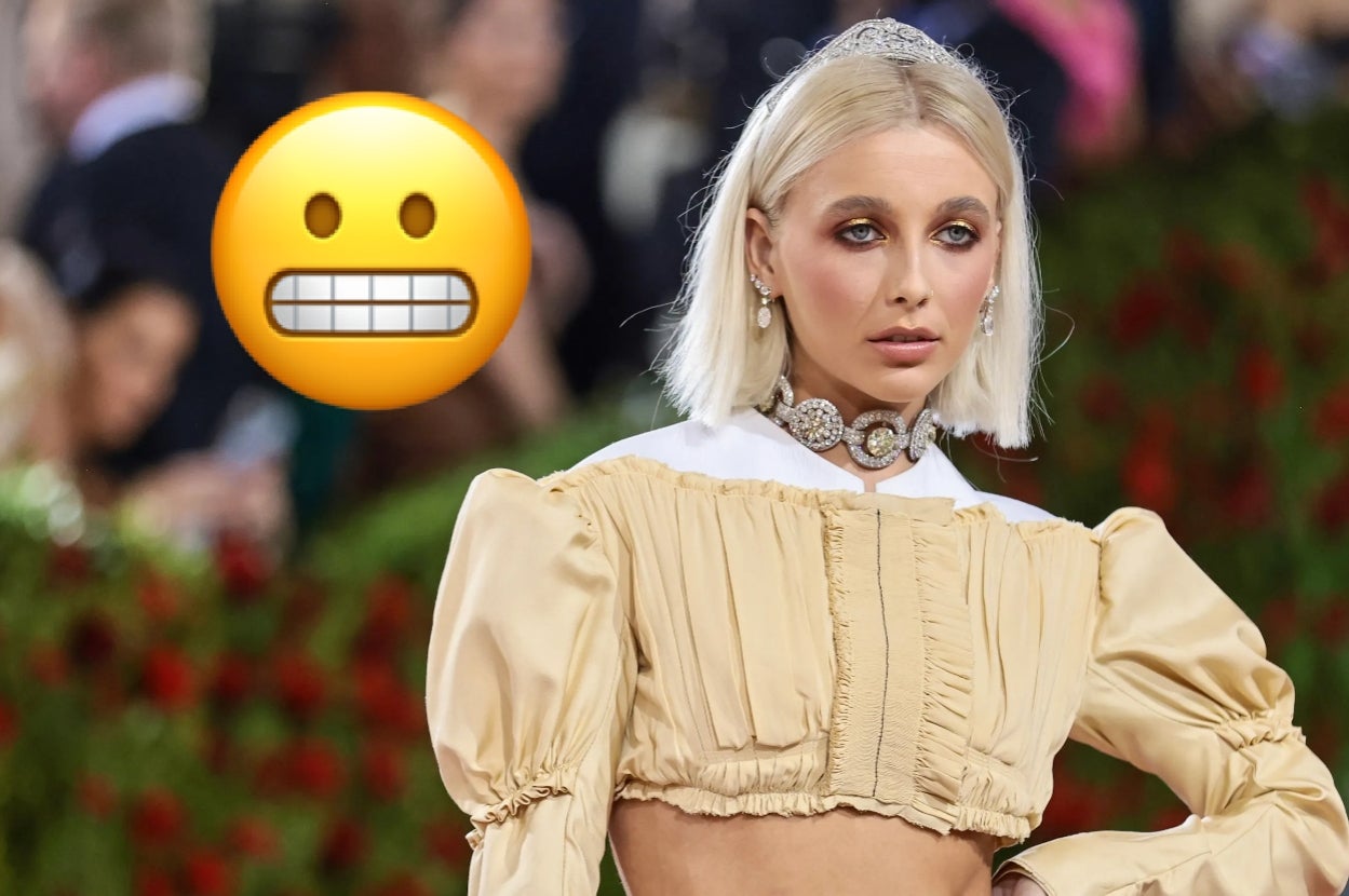 Person in puff-sleeve crop top with structured bodice on red carpet, wearing jeweled headpiece and choker; grimacing emoji added