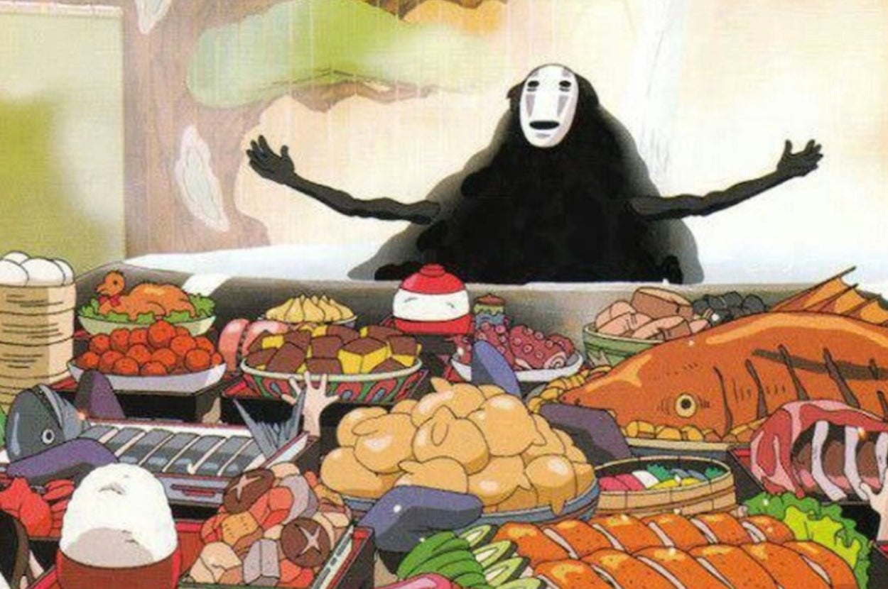 Animated character with a white mask and dark cloak behind a lavish spread of food, arms outstretched