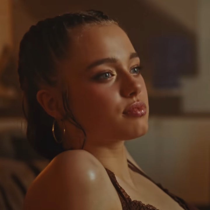 Person with braided hair and hoop earrings gazes thoughtfully, wearing an intricate top. The setting appears relaxed and intimate