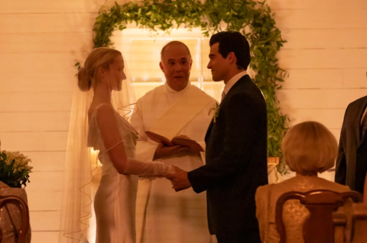 A bride and groom exchange vows at a wedding ceremony, with an officiant holding a book, in a warmly lit setting