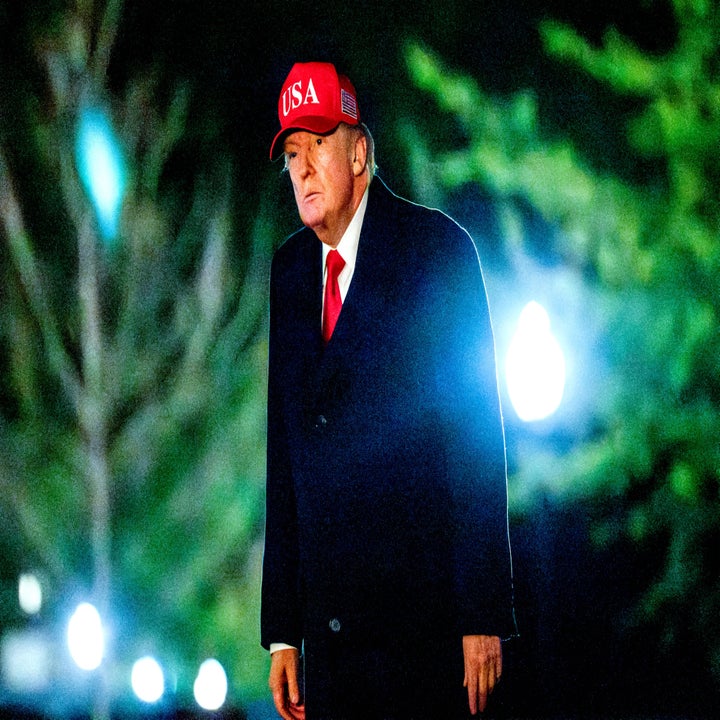Person in a dark coat and red "USA" cap stands outdoors, lit by bright lights at night