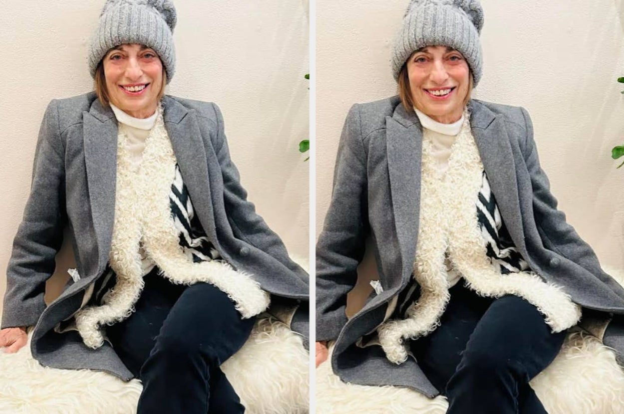 Person sitting and smiling, wearing a knit hat, gray coat over a textured sweater, and dark pants, evoking a cozy, casual vibe