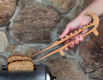 Person using wooden tongs to remove toast from a toaster against a stone wall background
