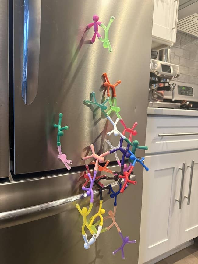 Colorful stick-figure magnets arranged climbing a refrigerator in a kitchen setting