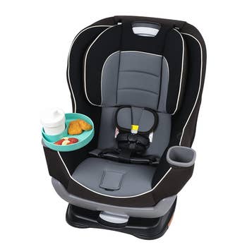 Child car seat with cup holder, featuring a secured safety harness and snack tray with nuggets and fruit