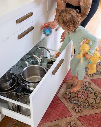 a model child going through a drawer of pots with another model holding the game that says