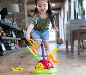 Child playing ring toss on floor with a colorful ladybug toy, indoors