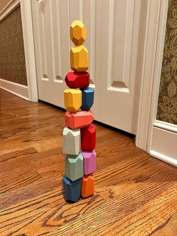 Stacked wooden block toys standing on a wooden floor in front of a white door, showcasing balance and creativity