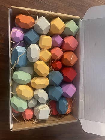 A box containing geometric, multifaceted stacking stones in various matte textures, used for balancing games or decoration