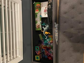 Rectangular storage bench open to reveal toys including a model building, dragon figures, and colorful building blocks