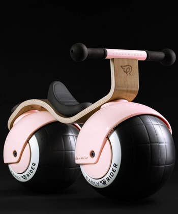 Innovative children's balance bike with a sleek, minimalist design featuring large black wheels and a curved wooden frame