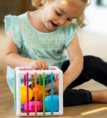 Child playing with a colorful activity cube, focused and engaged. The cube has different textures and shapes for interactive learning