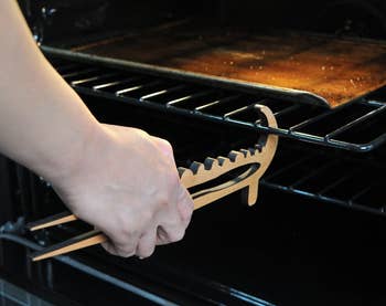 Person using wooden tongs to remove a hot baking tray from an oven