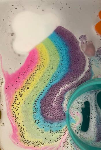 Rainbow bath bomb fizzing in water with a floating toy duck and a green cup