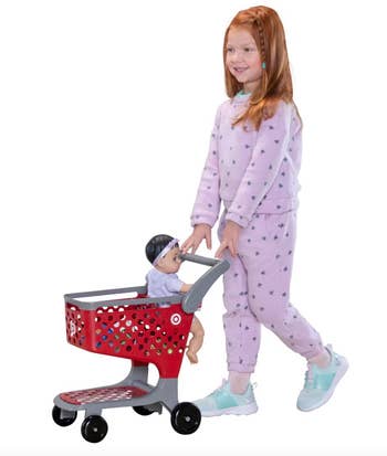 Child in a star-patterned outfit pushes a toy shopping cart with a doll inside